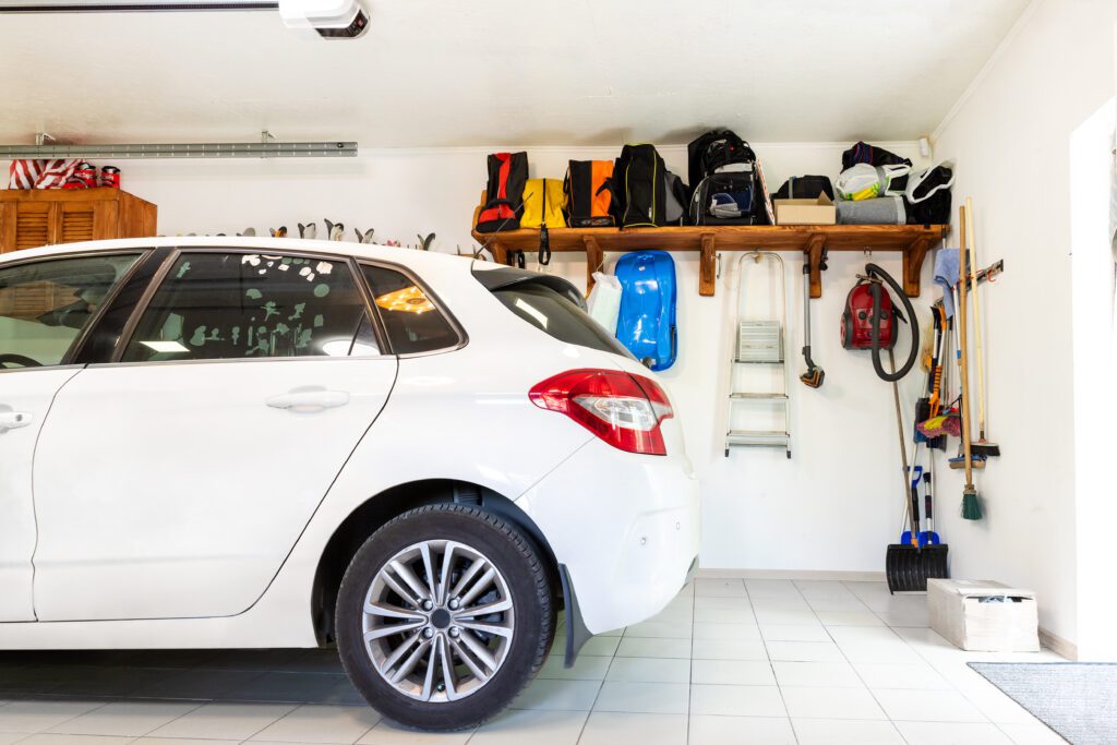 The rear end of a car is inside a garage with storage space behind it.