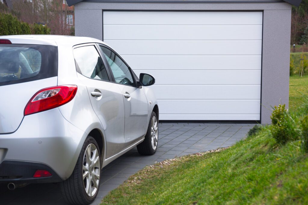 A silver car parked in front of a closed garage door.